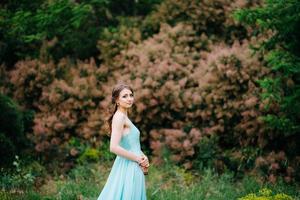 glückliches Mädchen in einem türkisfarbenen langen Kleid in einem grünen Park foto