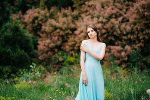 glückliches Mädchen in einem türkisfarbenen langen Kleid in einem grünen Park foto