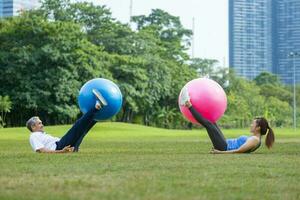 Senior asiatisch Mann und seine Tochter sind ausüben mit Yoga Ball im das Öffentlichkeit Park zu bauen Ader Körper Muskel zum ältere Langlebigkeit Übung und draussen trainieren Verwendungszweck foto