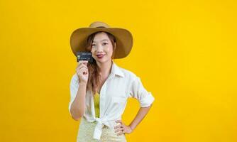 Porträt von jung asiatisch Frau im beiläufig Strand Kleidung mit Anerkennung Karte ist zeigen Verkauf Beförderung isoliert auf Gelb Hintergrund zum Reise und Mode Studio Schnitt aus Konzept foto