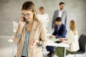 Frau, die am Telefon mit Mitarbeitern im Hintergrund spricht foto