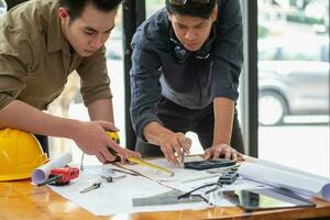 asiatisch Ingenieure Brainstorming und messen zu dokumentieren Kosten Schätzungen und schreiben Fußboden Pläne zum architektonisch und Ingenieurwesen Designs zum Häuser und Gebäude. foto