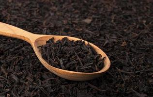 trockene Teeblätter im Holzlöffel lokalisiert auf dunklem Hintergrund foto