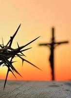 Dornenkrone von Jesus Christus gegen Silhouette des katholischen Kreuzes bei Sonnenunterganghintergrund