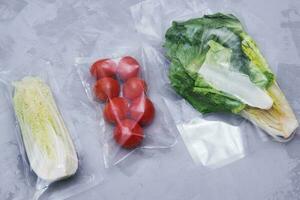 Tomaten, Grüner Salat Blätter und Peking Kohl im ein Vakuum Paket. ein einstellen zum liefern Essen zum Abendessen auf ein grau Hintergrund. foto
