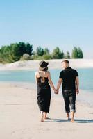 junges Paar ein Mann mit einem Mädchen in schwarzen Kleidern geht auf dem weißen Sand foto