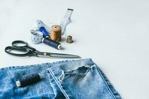 handwerk, Kleidung Reparatur. zerrissen Blau Jeans Nähen Zubehör Weiß Hintergrund. das Konzept von wirtschaftlich Dinge. foto