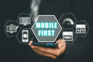 Mobile-First-Konzept, Personenhand mit Smartphone mit Mobile-First-Symbol auf virtuellem Bildschirm, digitales Marketing, Schreibtisch. foto