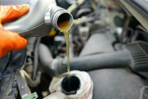 Gießen Öl zu das Wagen. Auto Mechaniker halten ein Flasche von Öl im Hand Über das Motor. Auto Motor Öl. Belag oben Auto Öl. foto