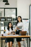 zwei asiatisch Geschäftsfrau diskutieren Investition Projekt Arbeiten und Planung Strategie mit Tablette Laptop Computer im Büro. foto