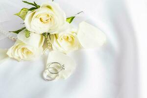 zwei schön Weiß Gold Diamant Engagement Ringe Lüge auf ein Tee Blatt Blütenblatt auf ein Pastell- Hintergrund mit frisch Blumen. ein Kopieren Raum. foto