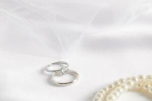schön Hochzeit Komposition zum das Design von Hochzeit Einladung, Album. zwei Ringe im Weiß Gold mit brillant auf ein schick Weiß Satin- mit ein Schleier. foto