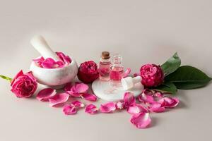 ein einstellen von natürlich Kosmetika zum Gesicht und Körper Haut Pflege basierend auf Rose Öl im verschiedene Flaschen und ein Granatwerfer mit ein Stößel und Rose Blütenblätter. foto