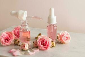 ein öffnen Flasche von Rose Öl und ein Pipette gefüllt mit Kosmetika auf ein Marmor Podium mit Blumen und Rose Blütenblätter. feuchtigkeitsspendend, Erweichung das Haut. foto