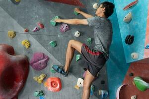 Mann Klettern auf Mauer Ausbildung im Fitnessstudio, aktiv sportlich männlich üben Felsen Klettern auf künstlich Felsen im extrem Sport, Bouldern, Klettern Wand, Bergsteiger ist Ausbildung, Felsen Klettern im das Stadt, stark foto