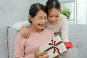 Mutter Tag, süß asiatisch Teen Mädchen geben Geschenk Box zu reifen Mitte Alter Mama. Liebe, Kuss, Pflege, glücklich Lächeln genießen Familie Zeit. feiern Besondere Gelegenheit, glücklich Geburtstag, glücklich Neu Jahre, fröhlich Weihnachten foto