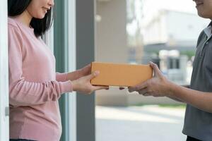 glücklich lächelnd Frau erhält Kisten Paket von Kurier im Vorderseite Haus. Lieferung Mann senden liefern äußern. online Einkaufen, Papier Behälter, wegbringen, Briefträger, Lieferung Service, Pakete foto