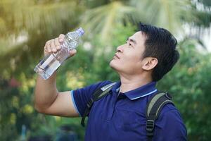 gut aussehend asiatisch Mann Reisender hält Flasche von Trinken Wasser zu trinken draußen. Konzept , Trinken Wasser zum Gesundheit, gesund lebensstil.löschen Durst, reduzieren Ermüdung, erfrischt Körper. foto