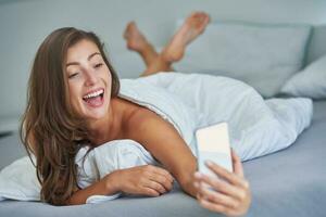 Brünette Frau auf Bett mit Telefon foto