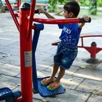 asiatisch Junge tun Routine Übung im Gesellschaft Park während das Morgen Zeit. süß wenig Kind Übung und Fitnessstudio zu behalten selbst passen zum Leben. Kinder Übung draussen schießen foto