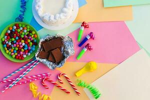 Kuchen, Süssigkeit, Schokolade, Pfeifen, Streamer, Luftballons auf Urlaub Tisch. Konzept von Kinder- Geburtstag Party. Aussicht oben. foto