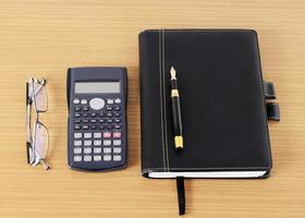 Füllfederhalter und Geschäftsbuch mit Taschenrechner und Brille auf hölzernem Schreibtisch für Büroarbeitsplatzkonzept foto