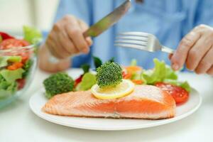 asiatisch Alten Frau geduldig Essen Lachs Anteil und Gemüse Salat zum gesund Essen im Krankenhaus. foto