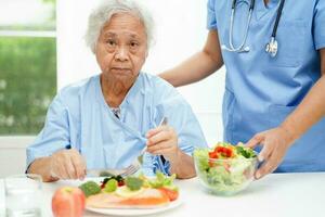 asiatisch Alten Frau geduldig Essen Lachs Anteil und Gemüse Salat zum gesund Essen im Krankenhaus. foto