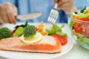 asiatisch Alten Frau geduldig Essen Lachs Anteil und Gemüse Salat zum gesund Essen im Krankenhaus. foto