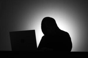 mysteriös Mann tragen schwarz Kapuzenpullover mit Laptop und halten Anerkennung Karte im das dunkel Zimmer. Hacker und Cyber Sicherheit Konzept. foto