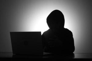 mysteriös Mann tragen schwarz Kapuzenpullover mit Laptop und halten Anerkennung Karte im das dunkel Zimmer. Hacker und Cyber Sicherheit Konzept. foto