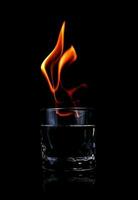 Glas mit Wodka und Feuerflammen auf einem schwarzen Hintergrund foto