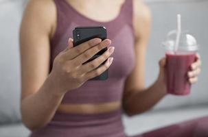 Fitness-Frau, die einen Entgiftungssaft mit einem Smartphone hat foto