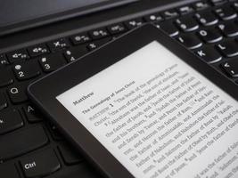 Nahaufnahme des E-Book-Readers mit der heiligen Bibel auf einer Laptoptastatur mit Sonnenstrahl-Lichtkonzept