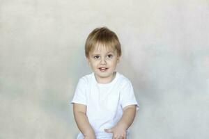 Porträt von ein süß wenig Junge im ein Weiß T-Shirt. Kinder- Emotionen. Kind auf das Hintergrund von das Mauer. Erfolg, hell Idee, kreativ Ideen und Konzepte. foto