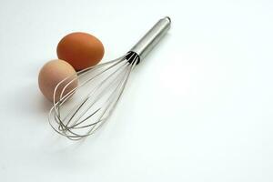 Fokus Hähnchen roh Eier und verwischen rostfrei Stahl Ei Schneebesen auf Weiß Hintergrund. Materialien oder Küche Ausrüstung zum Bäckerei. foto