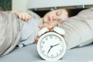 Junge liegt auf dem Bett und stoppt den Wecker am Morgen. Kinderhand greift nach dem Wecker, um ihn auszuschalten. foto