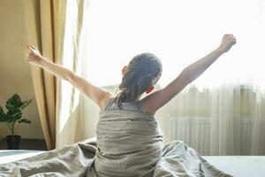 kleiner Junge sitzt und streckt sich morgens zu Hause im Bett auf einem Fensterhintergrund foto