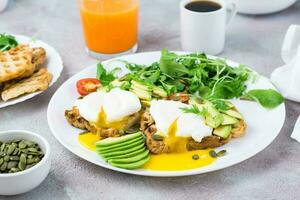 gesund Frühstück. Toast mit pochiert Eier, Scheiben von Avocado, Blätter und Kirsche Tomaten auf ein Teller und Saft und Kaffee auf ein serviert Tisch. Flexetarier Diät foto