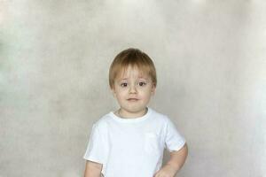 Porträt von ein süß wenig Junge im ein Weiß T-Shirt. Kinder- Emotionen. Kind auf das Hintergrund von das Mauer. Erfolg, hell Idee, kreativ Ideen und Konzepte. foto