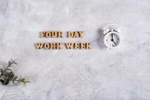 vier Tag Arbeit Woche Konzept mit hölzern Briefe und Alarm Uhr auf grau Hintergrund foto