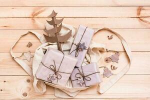 Weihnachten Geschenke eingewickelt im Kunst Papier und handgemacht Karton Baum im ein Einkaufen Tasche auf ein natürlich hölzern Hintergrund. umweltfreundlich Weihnachten Konzept. oben Aussicht foto