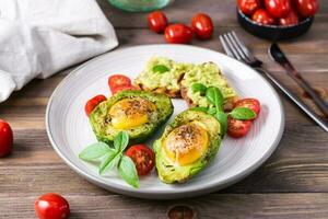 fertig für den Verzehr Vorspeise gebacken Avocado mit Ei, Toast und Kirsche Tomaten auf ein Teller auf ein hölzern Tisch. gesund Essen. Flexitarier Diät foto