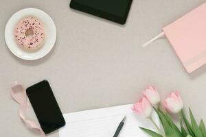 modisch stilvoll Rahmen zum ein weiblich Blogger, Freiberufler, Rosa Tagebuch, Tablette, Telefon, spenden auf ein Platte, Rosa Tulpen und ein öffnen Notizblock mit ein sauber Seite auf ein Kaffee Hintergrund mit Kopieren Raum foto