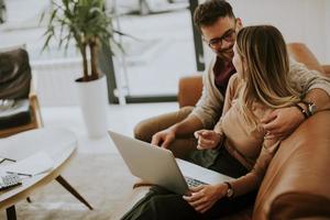 junges Paar mit Laptop zusammen beim Sitzen auf dem Sofa zu Hause foto