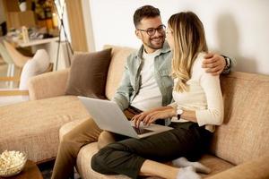 junges Paar mit Laptop zusammen beim Sitzen auf dem Sofa zu Hause