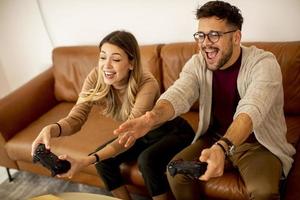 junges Paar, das zu Hause Videospiele spielt, auf Sofa sitzt und sich amüsiert