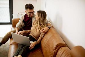 junges Paar mit Laptop zusammen beim Sitzen auf dem Sofa zu Hause