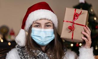 Porträt einer Frau, die Weihnachtsmütze und weißen Pullover in der medizinischen Maske trägt