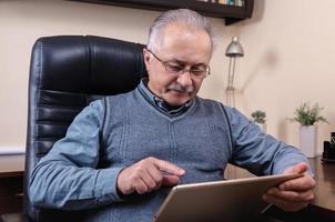 älterer Mann, der Nachrichten auf digitalem Tablett liest foto
